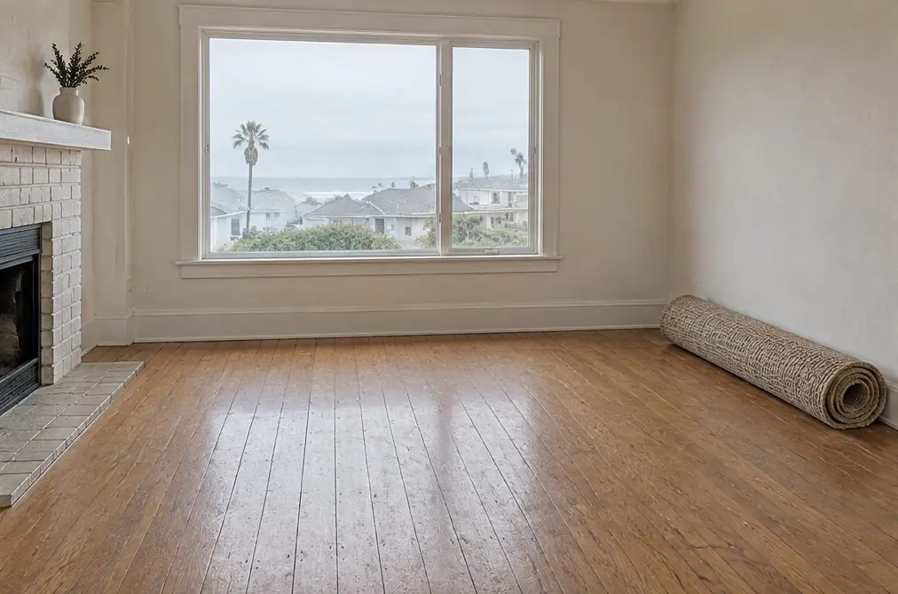 Illustration: an older Oxnard living room with a waxed oak strip floor, visible seams between the boards, a window with a coastal light and a rolled-up rug against the wall